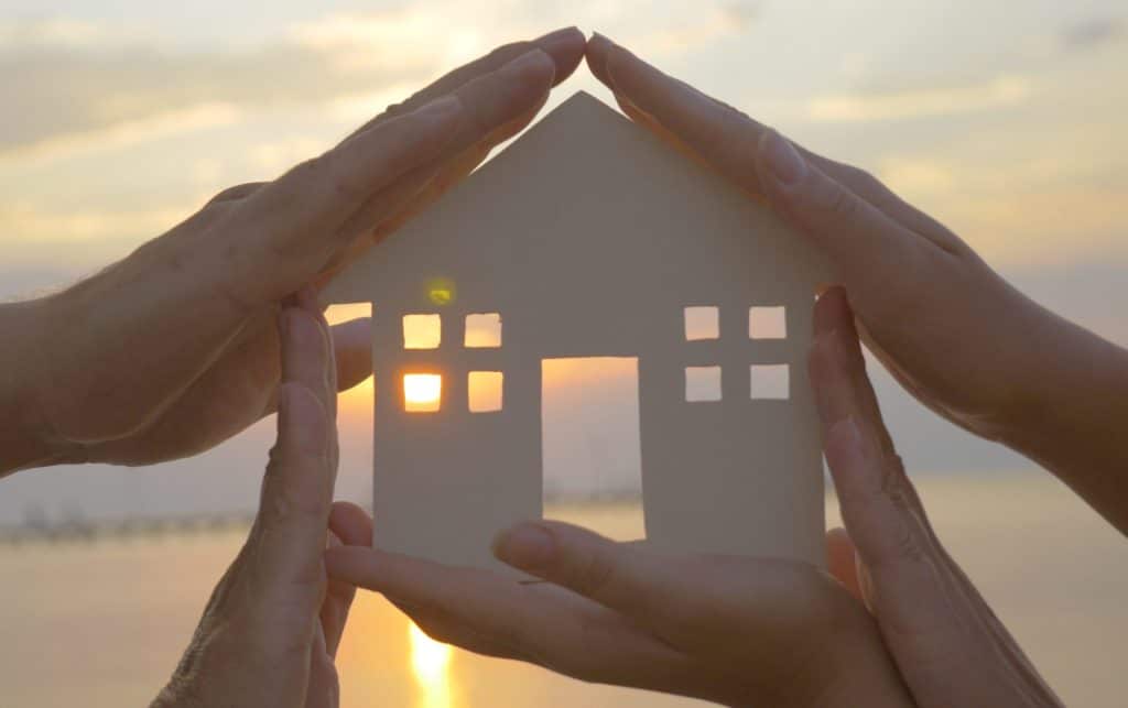 hands of a family displaying a paper cut out of a house