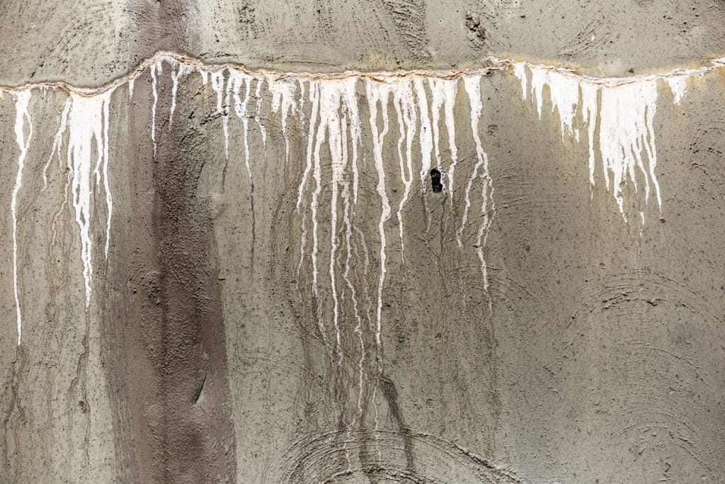 A concrete wall shows extensive white mineral deposits and vertical water stains, indicating signs of moisture intrusion or a possible slab leak.